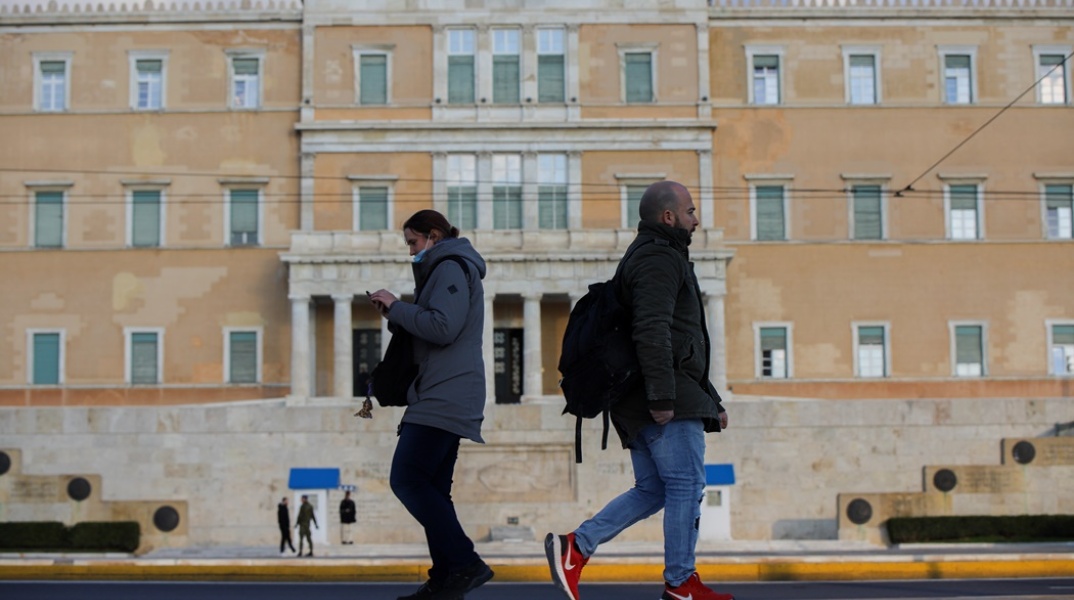 Άνδρας και Γυναίκα περπατούν στο κέντρο της Αθήνας με φόντο τη Βουλή των Ελλήνων