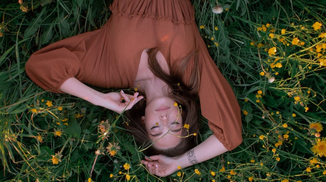 Ένα κορίτσι ξαπλώνει στο γρασίδι και ποζάρει. 