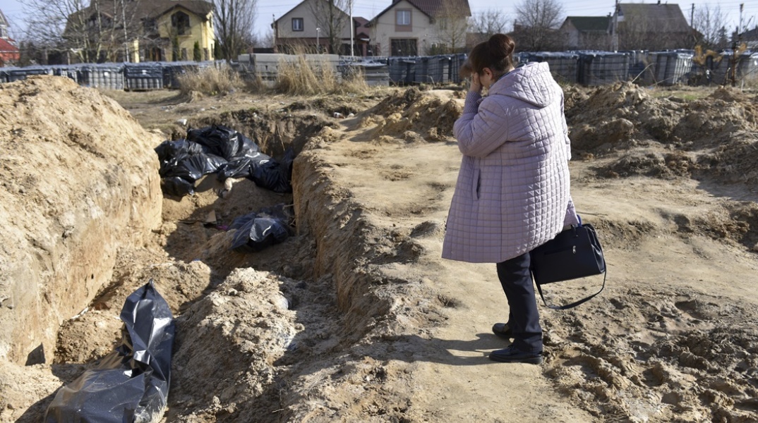 Γυναίκα στέκεται συγκλονισμένη πάνω από ομαδικό τάφο στην Μπούκα της Ουκρανίας