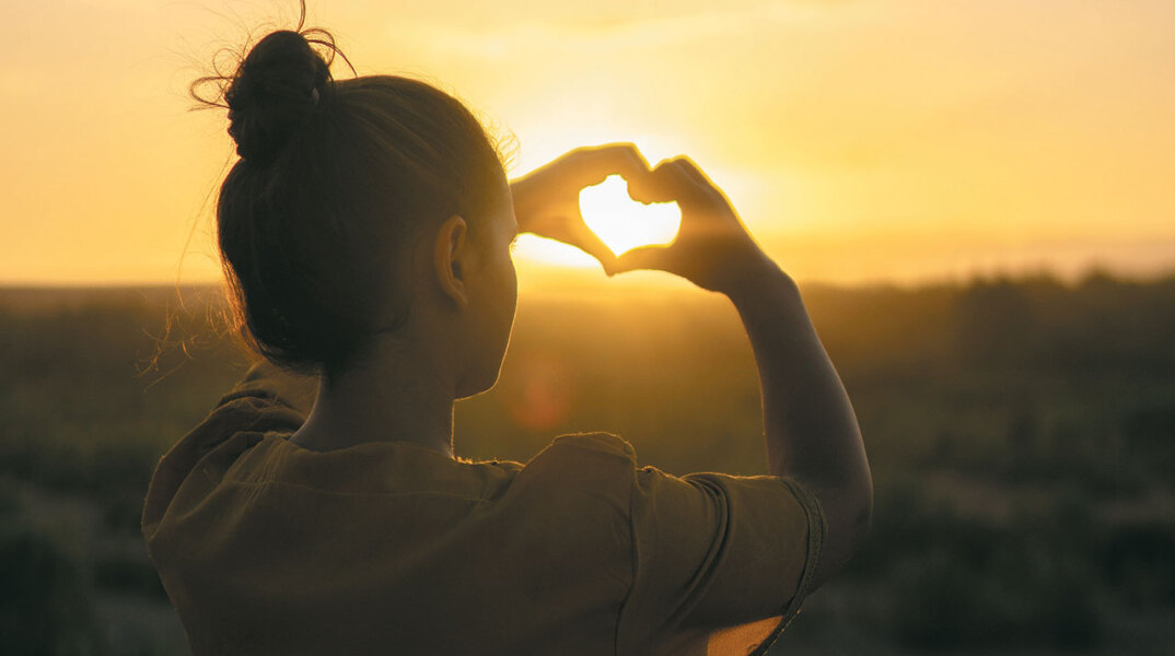 Κορίτσι σχηματίζει καρδιά με τα χέρια της με φόντο το ηλιοβασίλεμα
