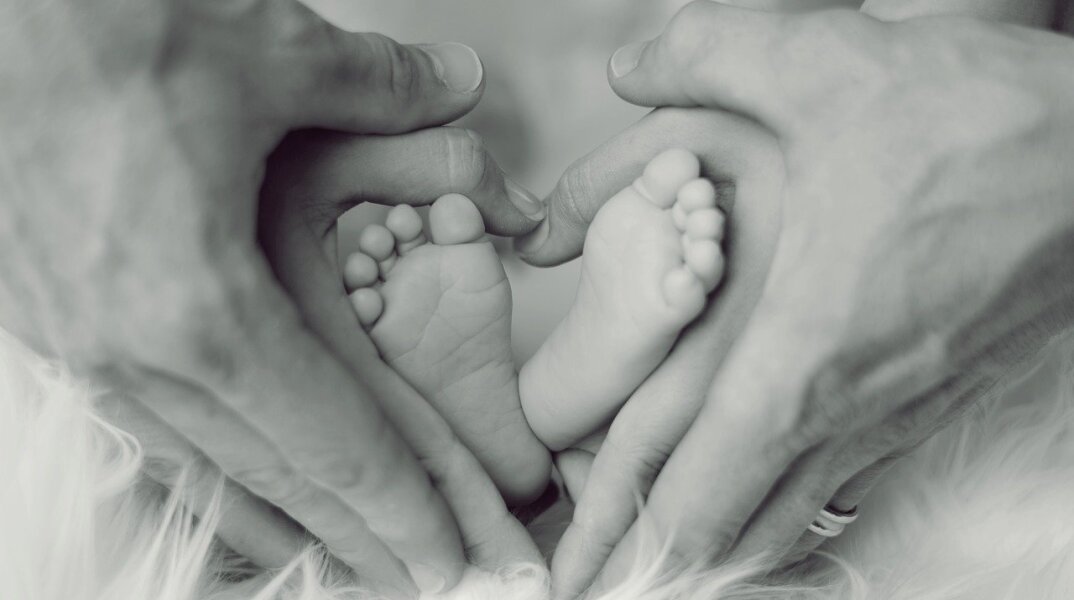 Ασπρόμαυρη φωτογραφία όπου γονείς κρατούν στα χέρια τους τις πατούσες του μωρού τους
