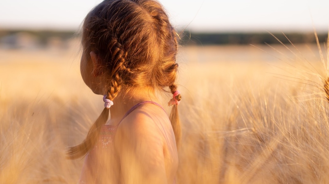 Κοριτσάκι με κοτσιδάκια ποζάρει με γυρισμένη πλάτη σε χωράφι με στάχια 
