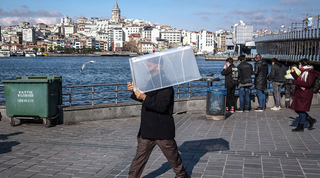 Άνδρας με μάσκα για τον κορωνοϊό στην Κωνσταντινούπολη μεταφέρει ένα πλαστικό κουτί