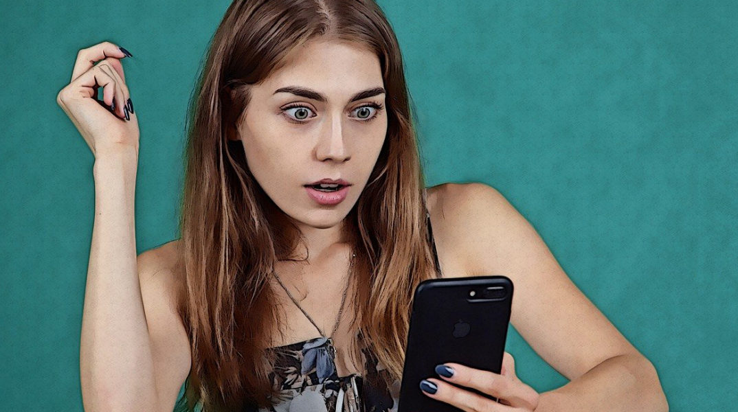 Γυναίκα κοιτάει σοκαρισμένη το κινητό της