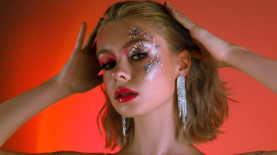 Κοπέλα με ξανθό καρέ μαλλί και στρας στο πρόσωπο που πιάνει το κεφάλι της