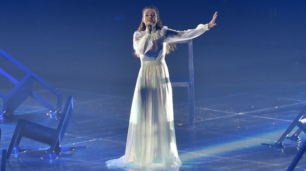 Η Αμάντα Γεωργιάδη στη σκηνή της Eurovision 2022 φορά μία δημιουργία της Σήλιας Κριθαριώτη και κρατά το μικρόφωνο ερμηνεύοντας το Die Together