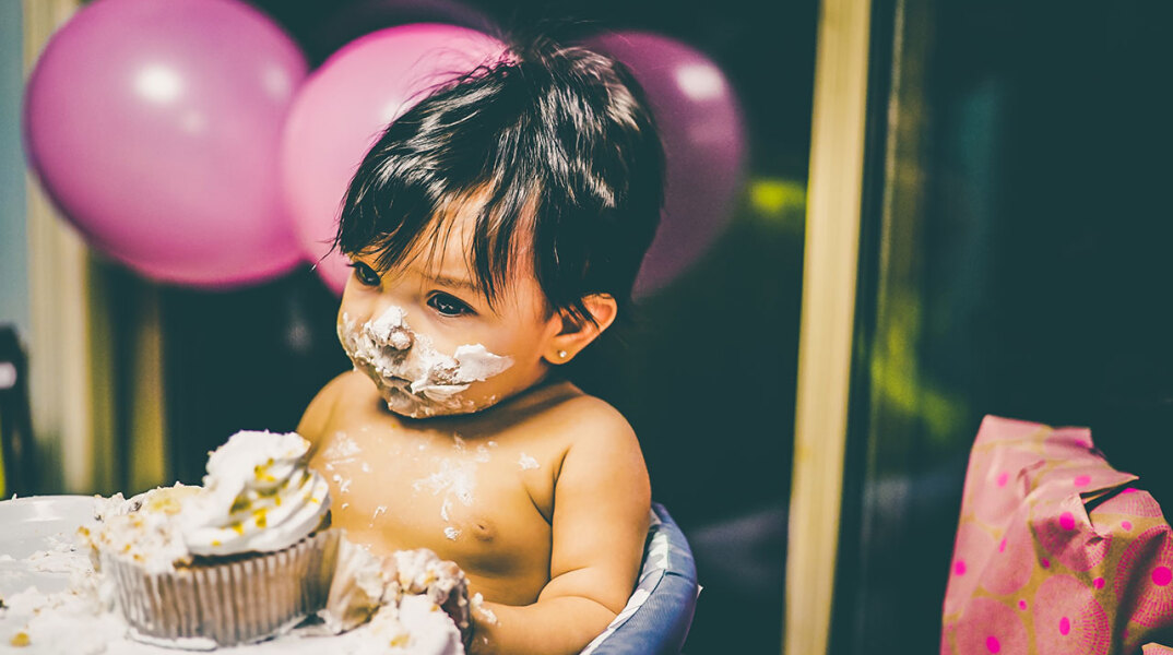Γυμνό παιδάκι σε καρεκλάκι ταΐσματος πασαλειμμένο με τούρτα στο πρόσωπο