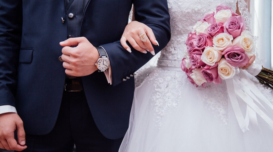 Γαμπρός κρατά αγκαζέ τη νύφη - Στη φωτογραφία διακρίνεται η ανθοδέσμη