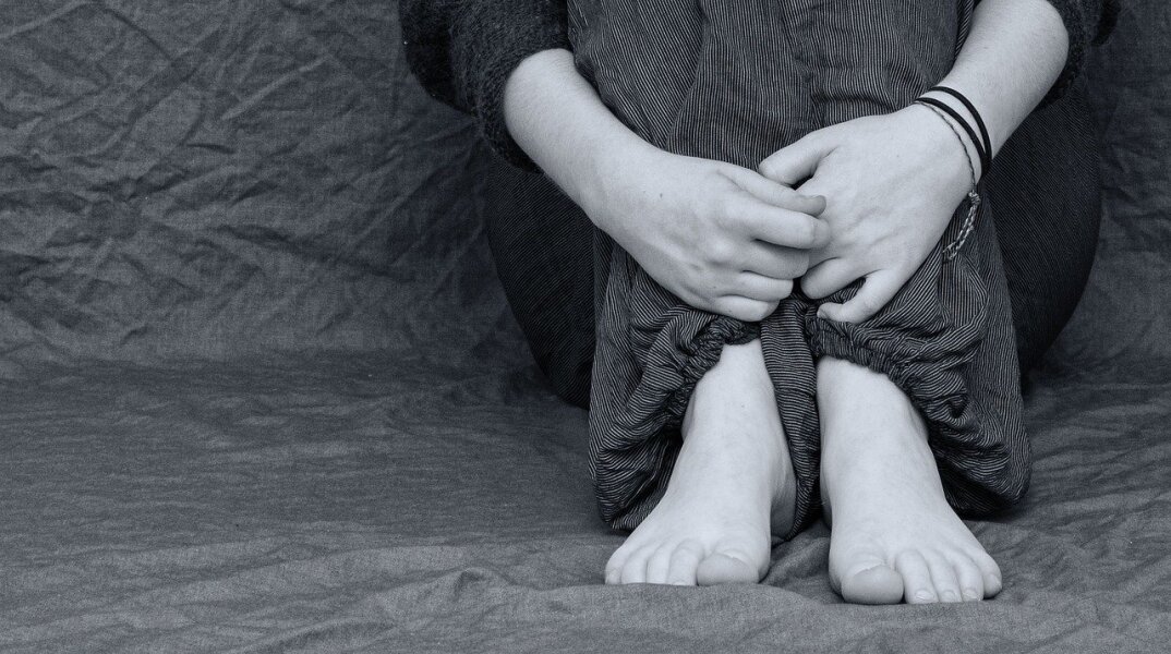 Παιδί καθιστό με σταυρωμένα χέρια μπροστά από τα πόδια - Δεν φαίνεται το πρόσωπό του - Εικόνα που παραπέμπει σε bullying ή κακοποίηση