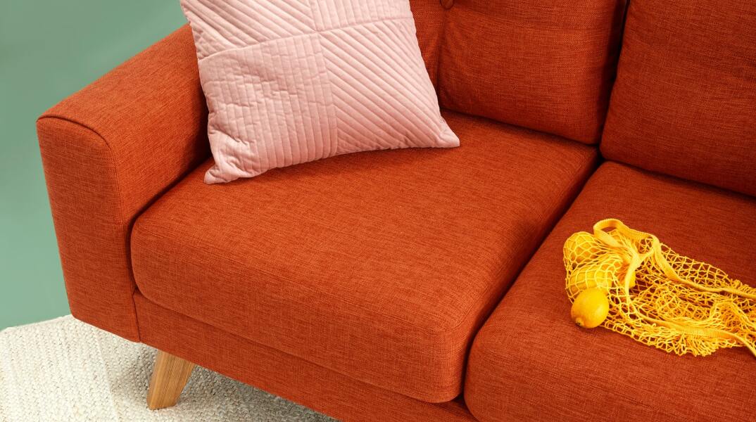 Καναπές σε χρώμα μεταξύ κόκκινου και πορτοκαλί πάνω στον οποίο υπάρχουν πορτοκάλια