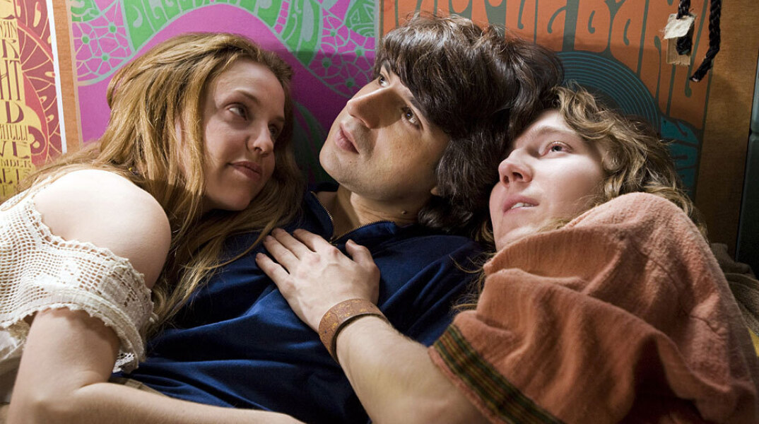 Δύο γυναίκες κι ένας άνδρας ξαπλωμένοι σε κρεβάτι 