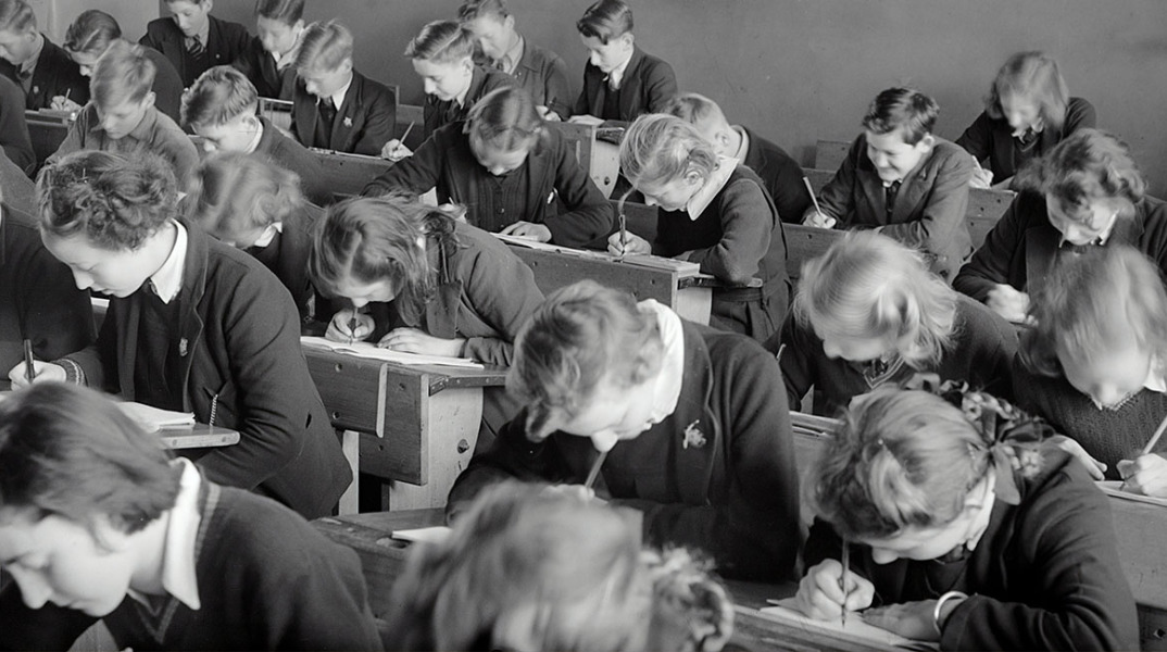 Ασπρόμαυρη φωτογραφία μαθητών σε θρανία να γράφουν διαγώνισμα