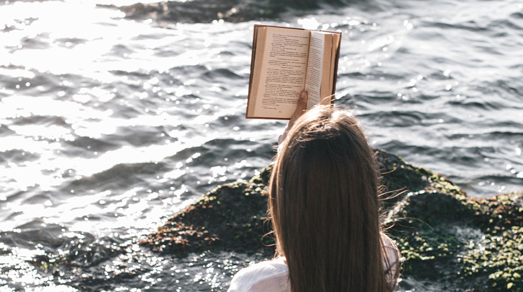 Κοπέλα που διαβάζει βιβλίο στη θάλασσα