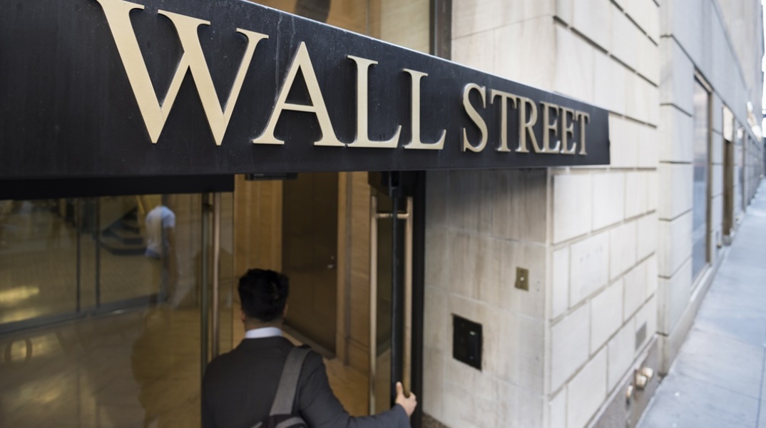 Άνδρας με κουστούμι και σακίδιο στην πλάτη ανοίγει την πόρτα της Wall Street στη Νέα Υόρκη