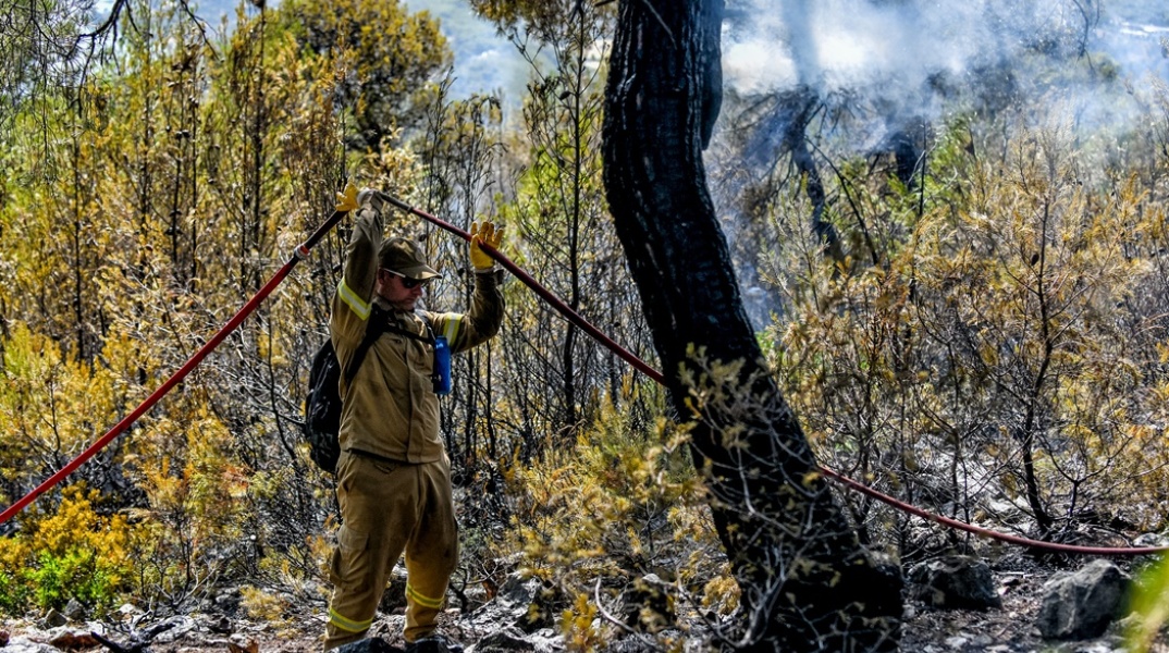 Φωτογραφία όπου πυροσβέστης πατά σε καμένα και κρατά ψηλά με τη μάνικα