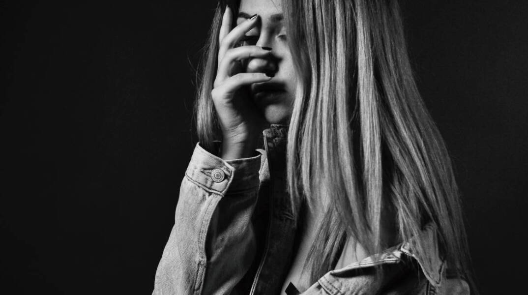 Ασπρόμαυρη φωτογραφία κοπέλας που κρύβει το πρόσωπό της με το χέρι της