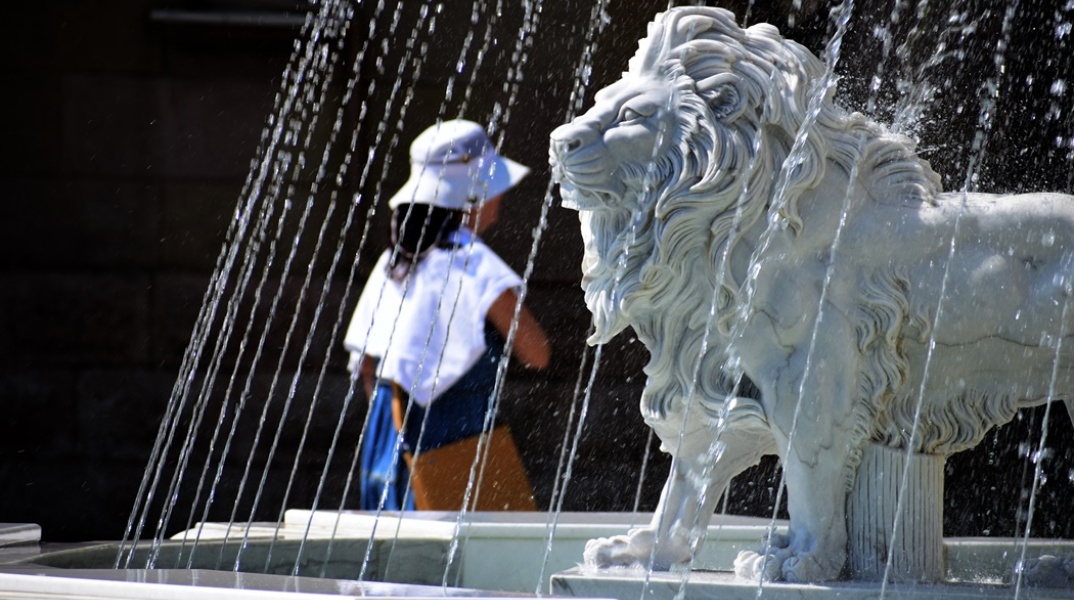 Λιοντάρι σε σιντριβάνι και γυναίκα με καπέλο προστατεύεται από τον καύσωνα