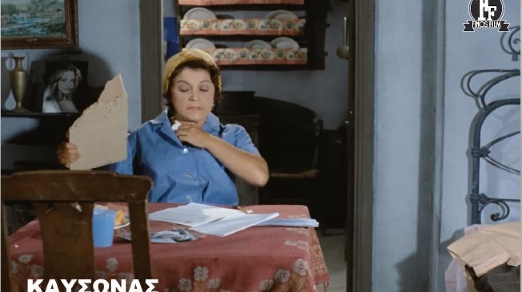 Η Ρένα Βλαχοπούλου κάνει αέρα με ένα χαρτόνι και κρατά ένα χαρτί για να σκουπίσει τον ιδρώτα της