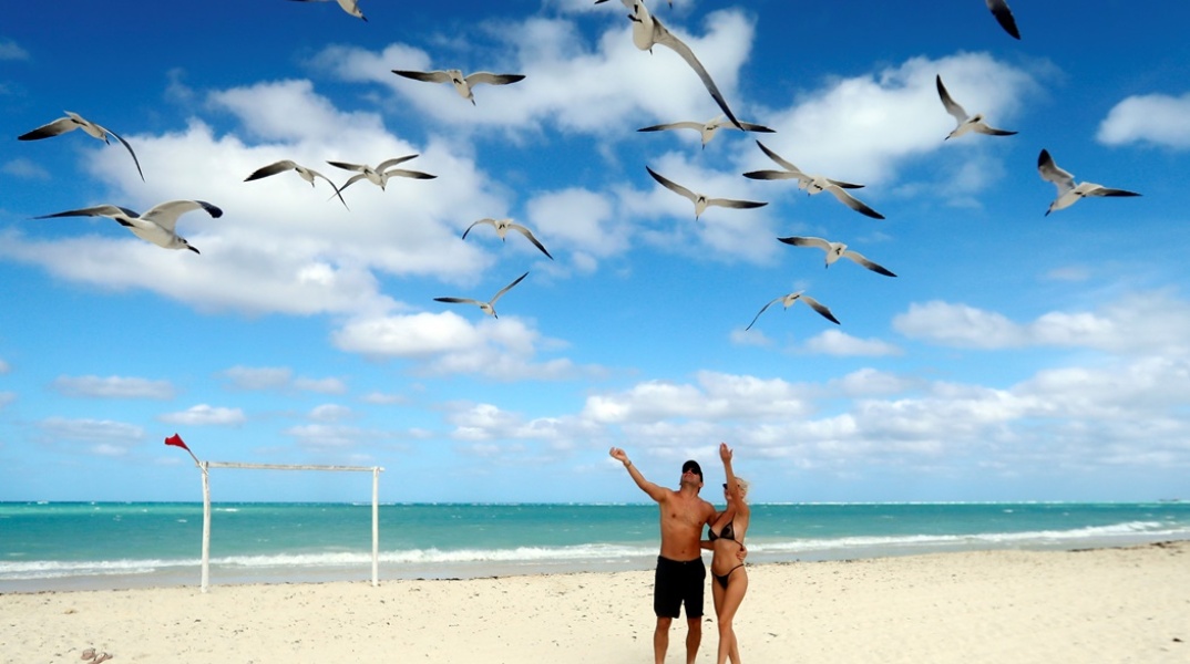 Τουρίστες σε παραλία της Κούβας υψώνουν τα χέρια προς τους γλάρους που πετούν από πάνω τους