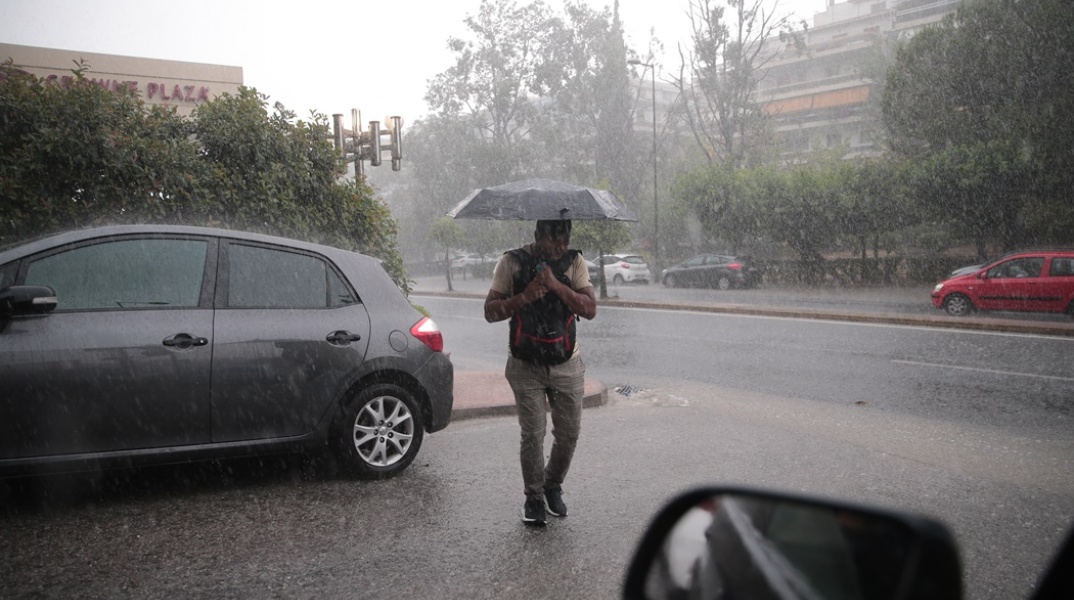 Άντρας με ομπρέλα περπατάει κατά τη διάρκεια έντονης βροχόπτωσης στην Αθήνα