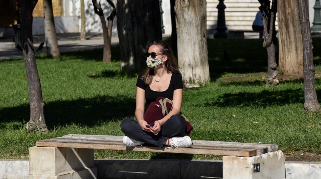 Κοπέλα που φορά μάσκα καθισμένη στο παγκάκι στο κέντρο της Αθήνας