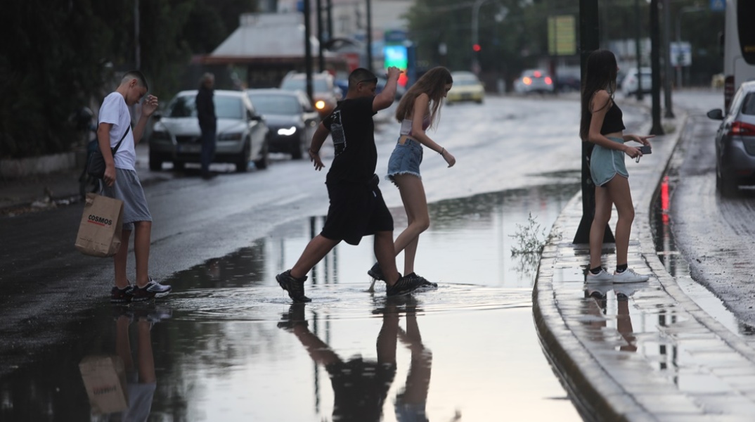 Πολίτες τρέχουν σε πλημμυρισμένο δρόμο υπό καταιγίδα