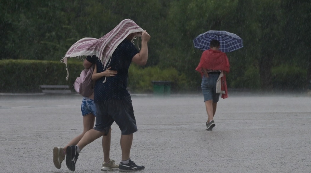 Πολίτες προστατεύονται από τη βροχή με πανωφόρι ή ομπρέλα