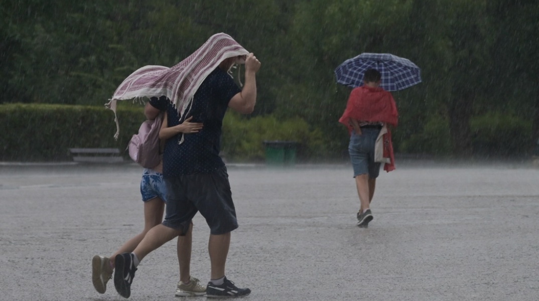 Πολίτες προστατεύονται από τη βροχή με πανωφόρι ή ομπρέλα
