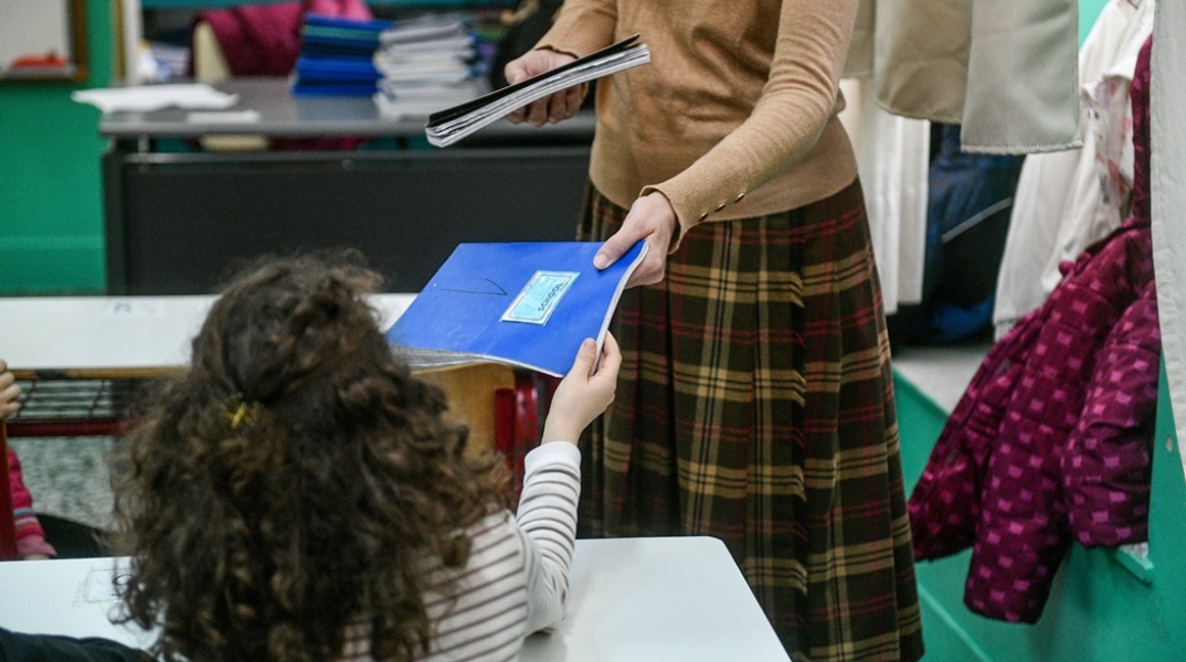 Μαθήτρια παίρνει το τετράδιο της από τη δασκάλα της σε αίθουσα δημοτικού σχολείου