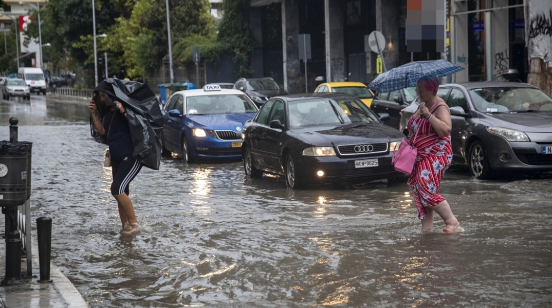 Πολίτες προσπαθούν να περάσουν πλημμυρισμένο δρόμο στη Θεσσαλονίκη και να προστατευτούν από τη βροχή