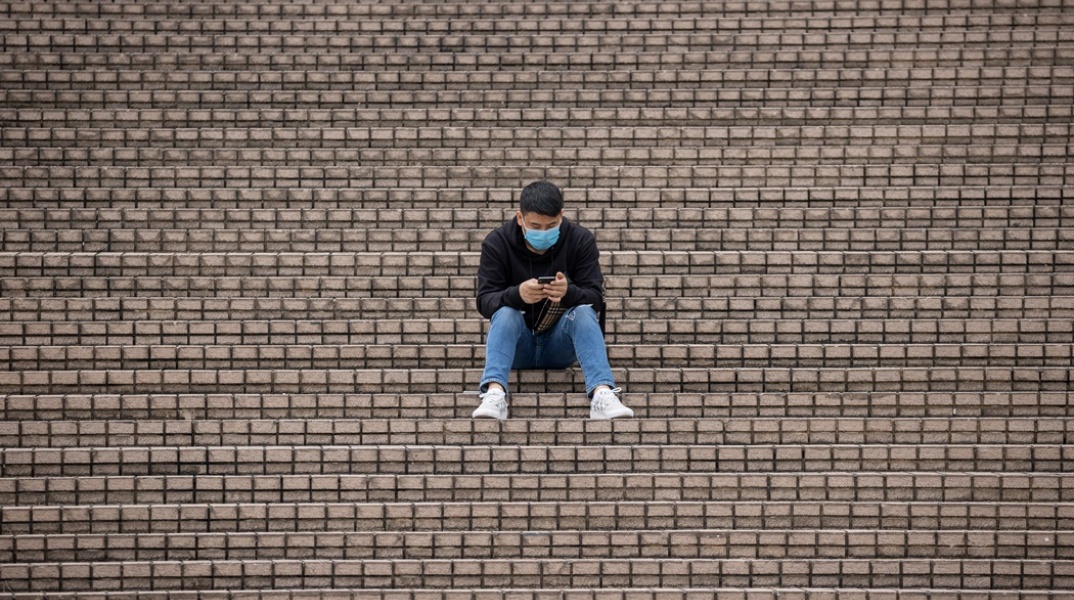 Πολίτης με μάσκα προστασίας από τον κορωνοϊό κάθεται σε σκαλιά