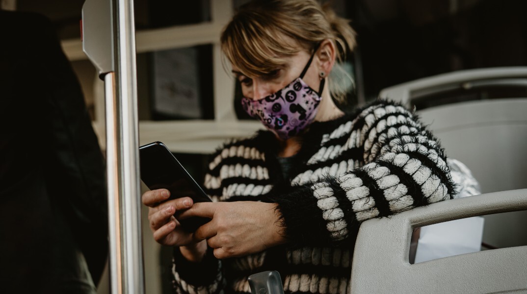 Γυναίκα με μάσκα κοιτάζει το κινητό της