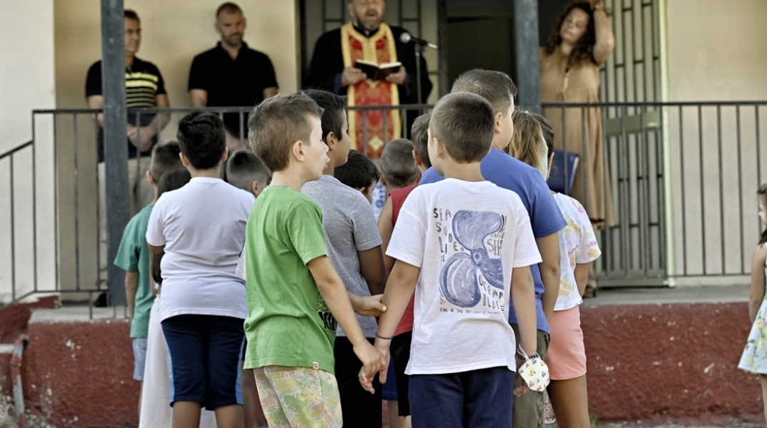 Μαθητές πιασμένοι χέρι χέρι κατά τη διάρκεια του αγιασμού από ιερέα σε προαύλιο σχολείου