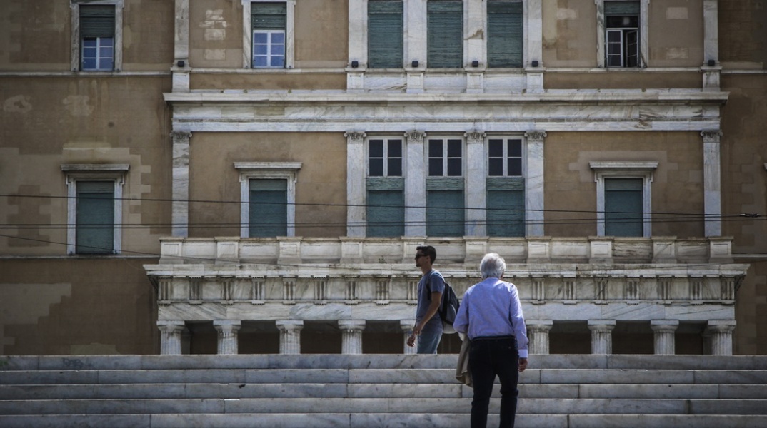Ηλικιωμένος ανεβαίνει τα σκαλιά της πλατείας Συντάγματος, όσο νεαρότερος άνδρας περπατά μπροστά από τη Βουλή