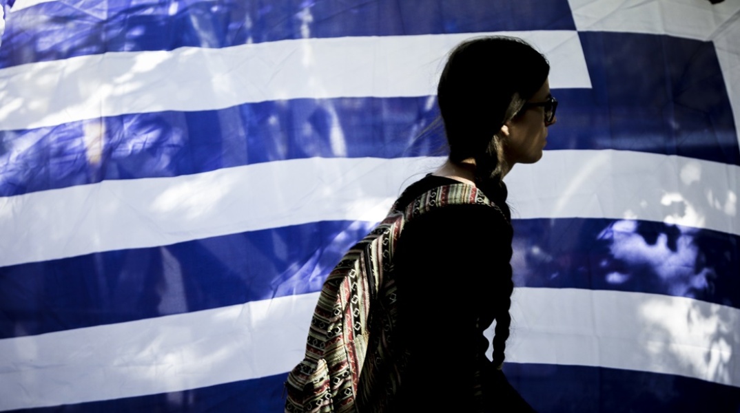 Ελληνική οικονομία Γυναίκα προχωρά μπροστά από ελληνική σημαία που κυματίζει