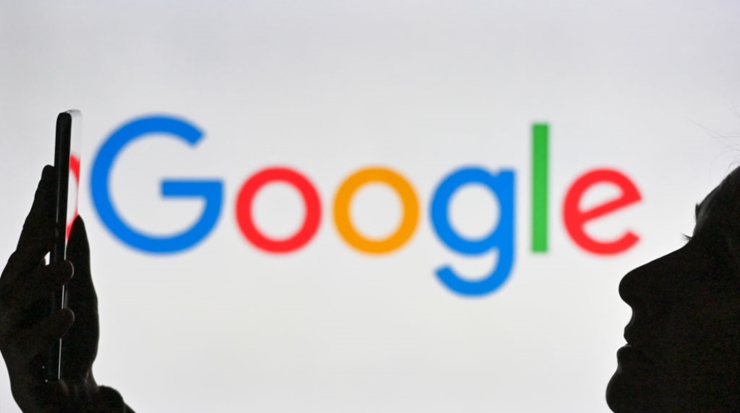 Άτομο κρατά ένα κινητό μπροστά από το λογότυπο της Google