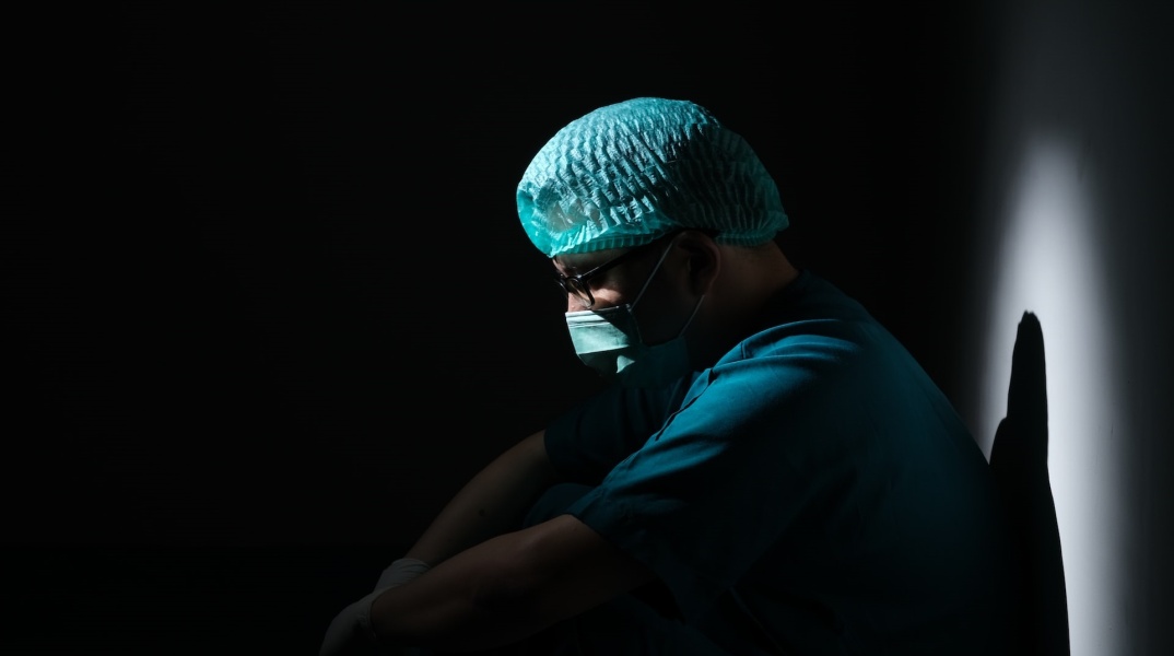 Γιατρός κουρασμένος φορά μάσκα και στέκεται στο ημίφως