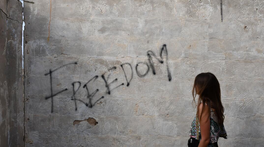 Κοπέλα κοιτάζει γκράφιτι σε τοίχο που γράφει «freedom»