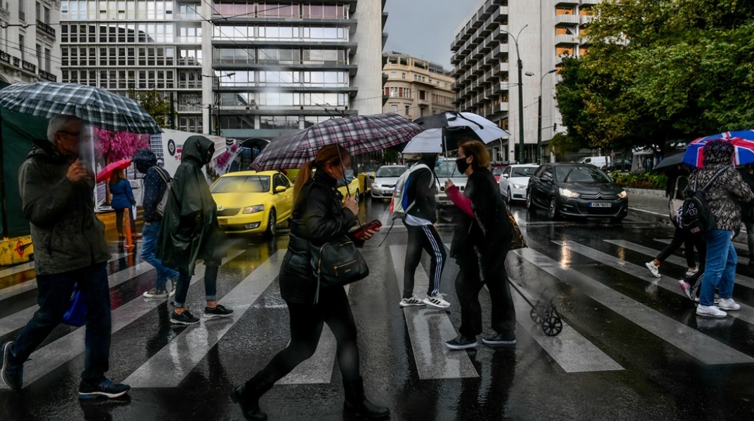 Πολίτες με ομπρέλα προστατεύονται από τη βροχή ενώ περπατούν σε δρόμο του κέντρου της Αθήνας