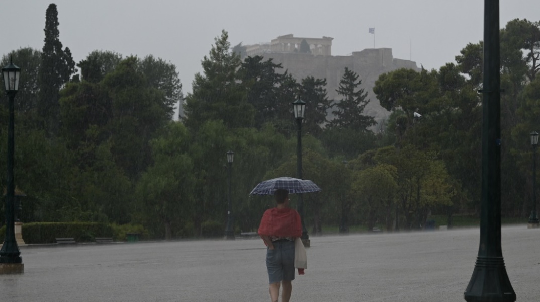 Άτομο σε δρόμο της Αθήνας κρατά ομπρέλα για να προστατευτεί από ισχυρή καταιγίδα