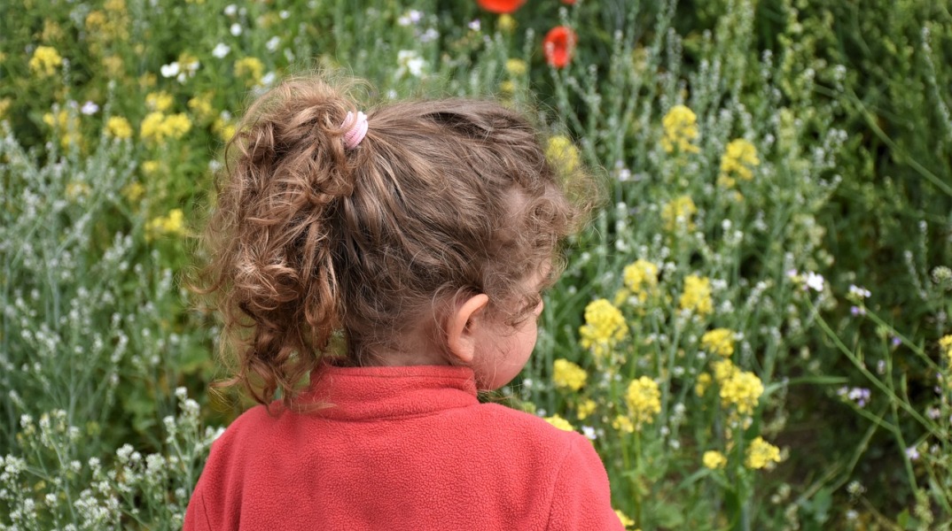 Παιδί ποζάρει γυρισμένο πλάτη έχοντας ως φόντο λουλούδια