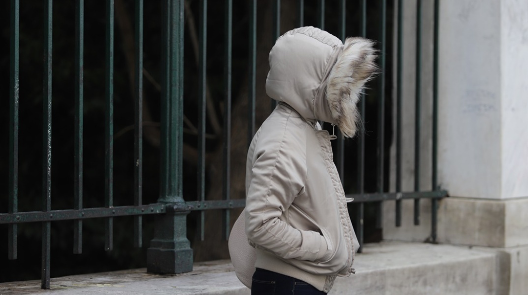 Γυναίκα προστατεύεται από το κρύο φορώντας μπουφάν και κουκούλα