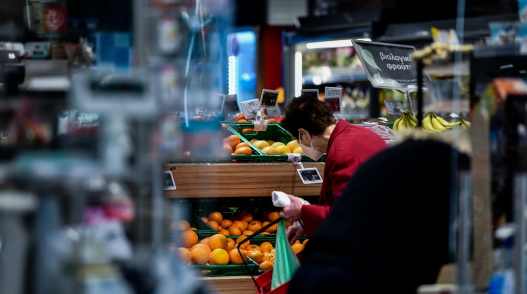 Γυναίκα ψωνίζει σε σούπερ μάρκετ φρούτα κρατώντας ένα κόκκινο καλάθι