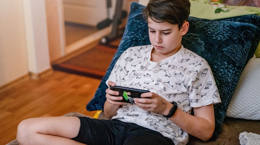 Έφηβος κρατά το κινητό του ενώ κάθεται σε μαξιλάρια