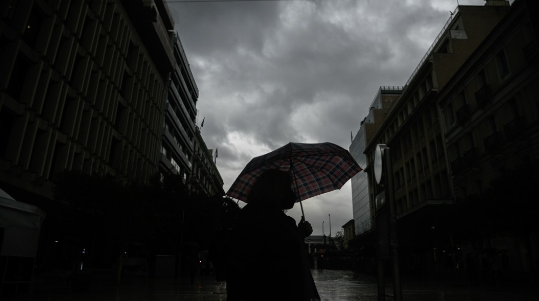 Γυναίκα προστατεύεται από ομπρέλα ενώ περπατά υπό καταιγίδα