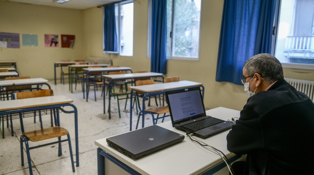 καθηγητής μέσα σε σχολική αίθουσα κάνει μάθημα μέσω τηλεκπαίδευσης