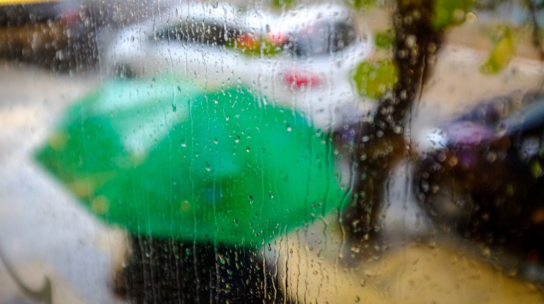 Τζάμι με σταγόνες από βροχή και μπροστά μία πράσινη ορμπέλα