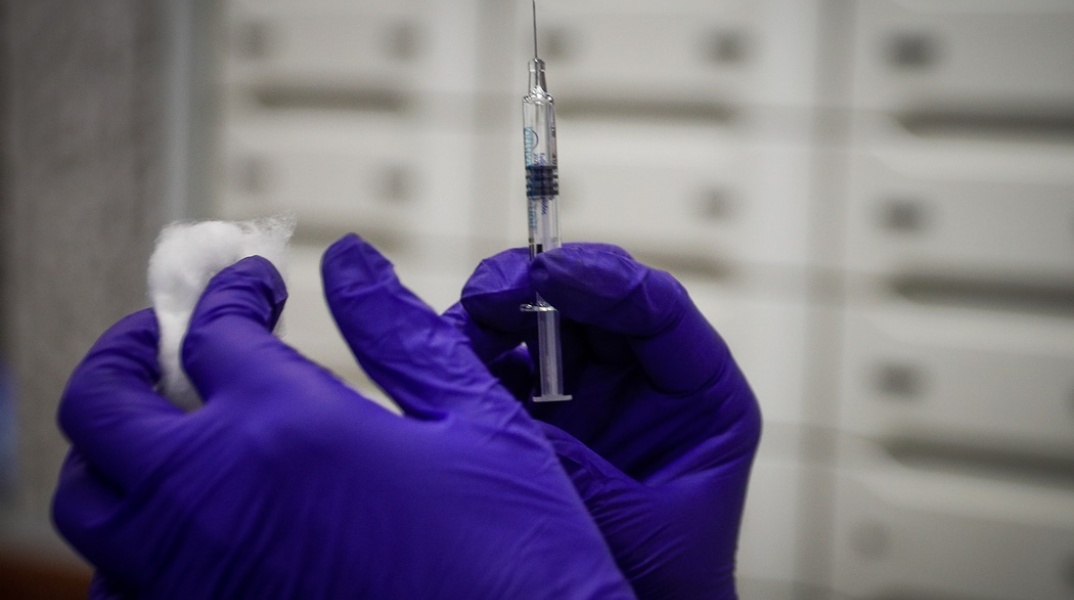 Γυναίκα με γάντια κρατά βαμβάκι και εμβόλιο κατά της γρίπης