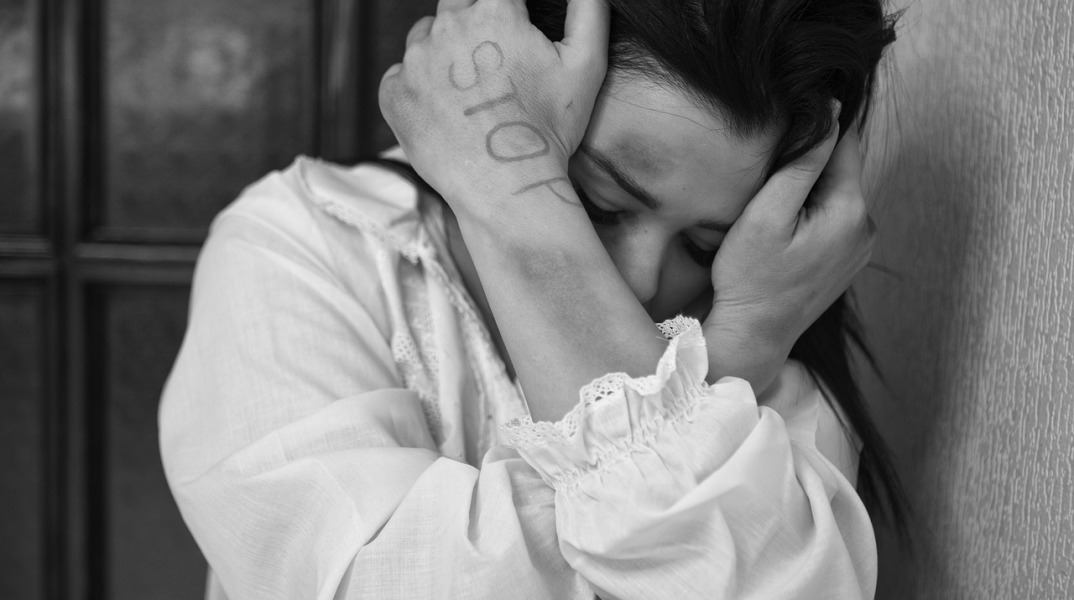 Κακοποιημένη γυναίκα προστατεύει το πρόσωπό της με τα χέρια της, στο ένα εκ των οποίων γράφει STOP