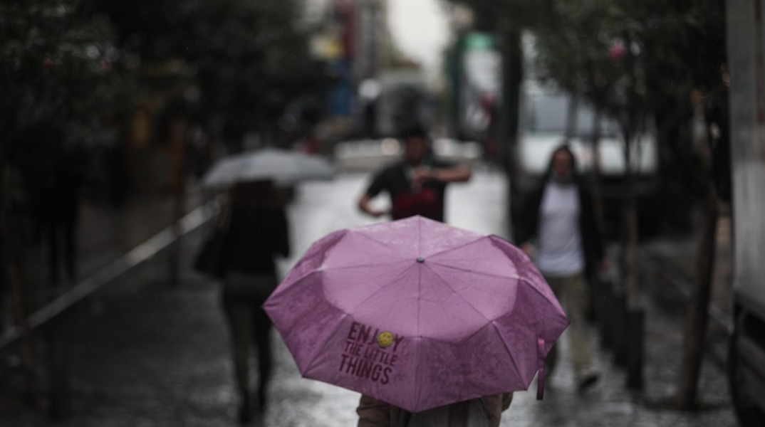 Γυναίκα κρατά ανοιχτή ομπρέλα για να προστατευτεί από τη βροχή
